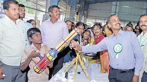 அதிக ஒலி எழுப்பி வனவிலங்குகளை விரட்ட மாணவர்கள் தயாரித்த துப்பாக்கியின் பயன்பாடு குறித்து ஆய்வு செய்யும் கிருஷ்ணகிரி மாவட்ட ஆட்சியர் பிரபாகர்.