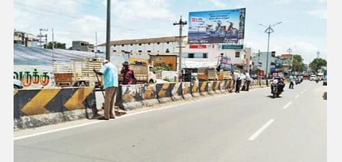 தருமபுரி நகரில் சாலைகளில் தேங்கிய மண்ணை, பாதுகாப்பு ஏற்பாடுகளின்றி அகற்றும் பணியில் ஈடுபட்டுள்ள நெடுஞ்சாலைத் துறை பணியாளர்கள்