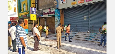 கோவை கிராஸ்கட் சாலை பகுதியில் மூடப்பட்டுள்ள கடைகளுக்கு முன் கிருமிநாசினி தெளிக்கும் பணியில் ஈடுபட்டுள்ள மாநகராட்சிப் பணியாளர்கள்.﻿