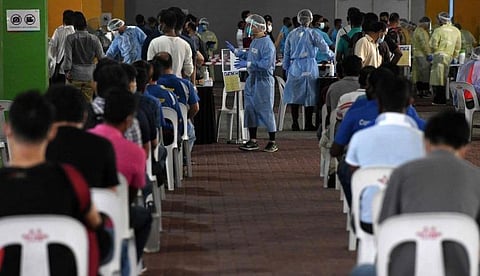 கரோனா பரிசோதனைக்காக அமர்ந்திருக்கும் தொழிலாளர்கள்