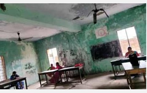 இடிந்து விழும் நிலையில் உள்ள வகுப்பறைக் கட்டிடத்தில் அமர்ந்து பணியாற்றும் ஆசிரியர்கள்.