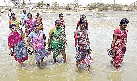 படகில் பயணம் செய்வதற்காக, முழங்கால் அளவு நீரில் நடந்து செல்லும் பெண்கள். படம்: ம.பிரபு