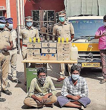 தக்காளி மூட்டைக்குள் மதுபாட்டில்கள் கடத்தியதாக கைது செய்யப்பட்ட இருவருடன் திருக்கோவிலூர் போலீஸார்.