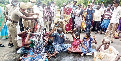 தி.மலை ஆட்சியர் அலுவலகம் முன்பு  தற்கொலைக்கு முயன்ற பரமசிவம் குடும்பத்தினர் மீது தண்ணீரை ஊற்றி காப்பாற்றிய காவல் துறையினர்.படம்: இரா.தினேஷ்குமார்.