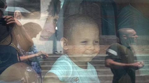 உக்ரைனில் உள்ள கிராமடோர்ஸ்கில் இருந்து வெளியேற தயாராகிக் கொண்டிருக்கும்போது தனது அம்மாவுடன் மடியில் அமர்ந்தபடி சிரிக்கும் சிறுவன்.