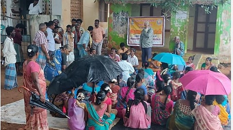 தொட்டிக்குப்பத்தில் மழையில் குடைபிடித்தபடி கிராமசபைக் கூட்டத்தில் பங்கேற்ற கிராம மக்கள்