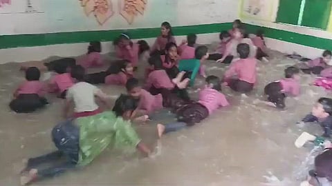 வகுப்பறையில் அமைக்கப்பட்ட நீச்சல் குளத்தில் விளையாடும் பள்ளிக் குழந்தைகள்.