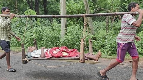 சாலை வசதி இல்லாததால் 14 கிமீ தூரம் தந்தையை கட்டிலில் சுமந்து மருத்துவமனையில் சேர்த்த மகன்