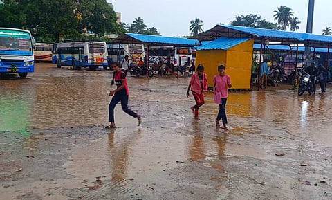 புதிய பேருந்து நிலைய கட்டுமானப் பணியால் அமைக்கப்பட்ட தற்காலிக பஸ் நிலையத்தில் சேறிலும், சகதியிலும் மழைநீரிலும் நடந்து சென்று பஸ் ஏறும் பயணிகள், குழந்தைகள்.