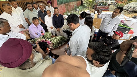 வீட்டுக்கு வெளியே கட்டிலில் அமர்ந்தபடி செய்தியாளர்களுக்கு பேட்டி கொடுக்கும் உதித் ராஜ்