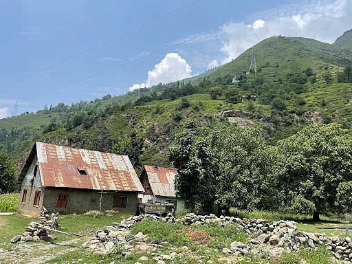 Old homes with rusted roofs stand near a new stone wall, showing the mix of old and new that now defines village life.