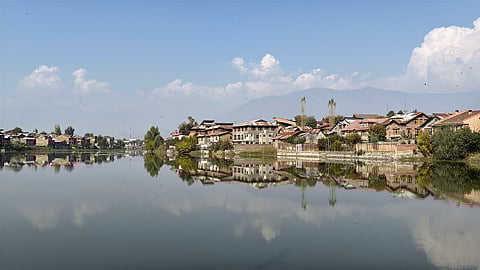 The calm waters of Khushal Sar perfectly mirror the houses and distant mountains, symbolizing the lake's rebirth.