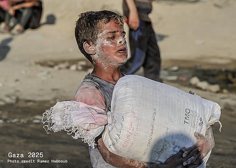 A starving child in Gaza covered in dust, carrying a heavy sack of flour.