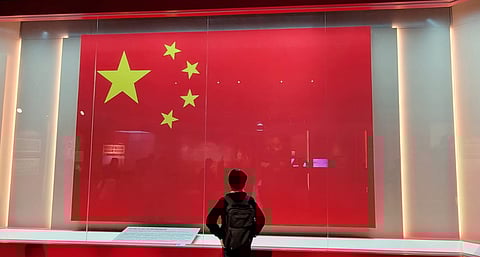 A visitor stands in front of a large flag of the People's Republic of China displayed behind glass at the Hong Kong Museum of History's National Security Exhibition Gallery.