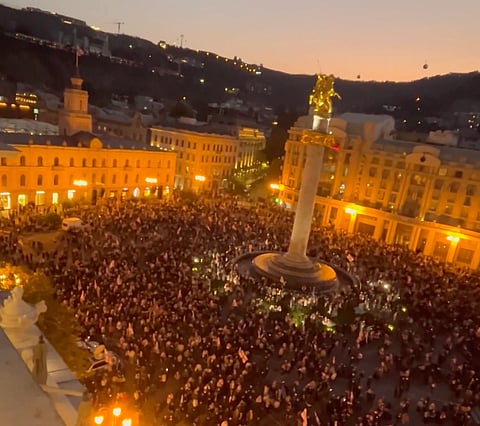 Thousands of protesters marching in Tbilisi's Freedom Square at dusk.