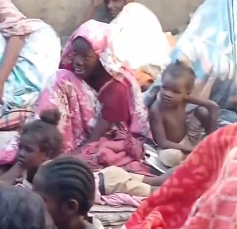 A group of Sudanese women and children in apparent distress, seated in an enclosed outdoor area.