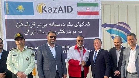 Kazakh and Iranian officials at the handover event in front of banners with both countries' flags and the KazAID logo.