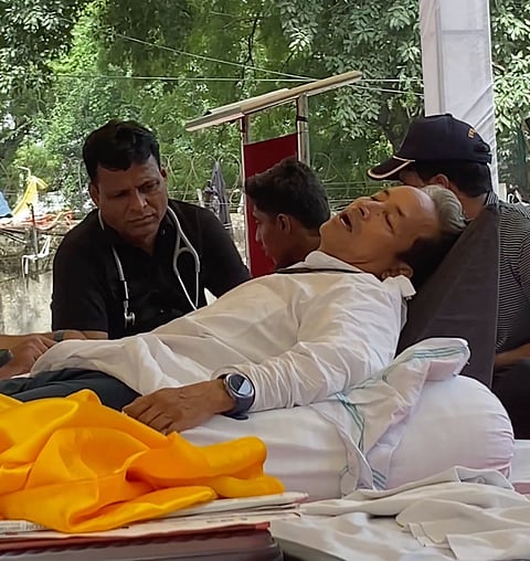 Wangchuk lying on a bed, surrounded by supporters and a doctor monitoring him.