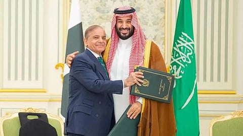 Two leaders in formal attire exchanging a document, with national flags and ornate decor.