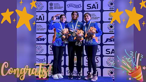 Three female shooters on a podium with medals and mascots.