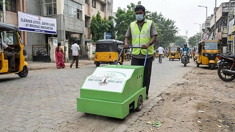 Worker uses green mobile cleaning machine on a city street.