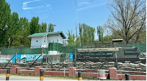 A snapshot of a watchtower and fencing that lines a military training camp along a major highway from Srinagar to Anantnag, south Kashmir, in April 2025. The walls, covered in sandbags and barbed wire, are painted with cultural references to the beauty of the valley. A small hole appears to be lookout for a sniper.