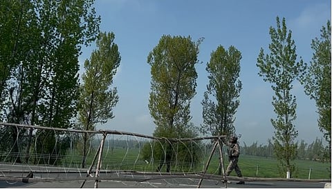 A major highway is separated by makeshift checkpoint. An officer stops traffic on a road in Kashmir in April 2025.