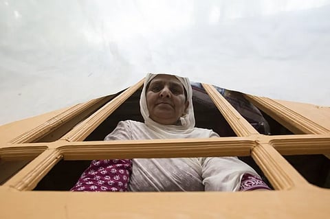Hafiza looks through a window covered with a polythene sheet. The family doesn’t have glass for their windows [Baba Tamim/Al Jazeera]
