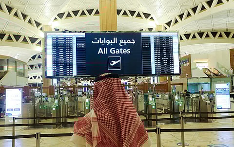 مسافر في مطار الملك خالد الدولي يتفقد تفاصيل الرحلة على لوحة المعلومات الإلكترونية.