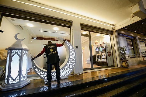 عامل في مقهى يرتب الزينة أمام المقهى قبل حلول شهر رمضان المبارك في بنغازي، ليبيا، 16 فبراير 2026