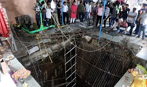 People stand around a structure built over an old temple well that collapsed in Indore