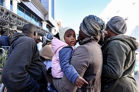 A child looks on while being carried by a woman as sub-Saharan African migrants seek refuge at UN's offices