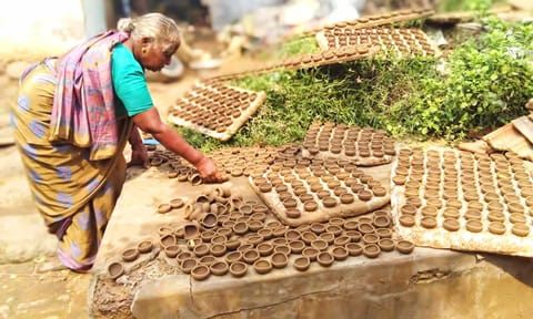 அகல்விளக்குகளை காய வைக்கும் பணியில் ஈடுபட்டுள்ள பெண்.