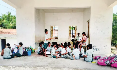 நாடக மேடையில் அமர்ந்து படிக்கும் பள்ளி மாணவ-மாணவிகள்.