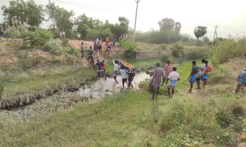 வாய்க்கால் வழியாக பிணத்தை கொண்டு செல்லும் காட்சி.