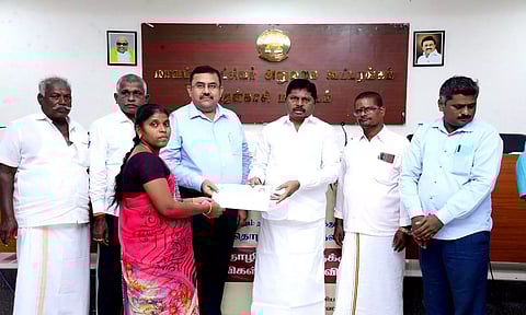 தமிழ்நாடு கட்டுமான தொழிலாளர் நலவாரிய தலைவர் பொன்குமார்  ஒரு பயனாளிக்கு உதவித்தொகை வழங்கிய காட்சி. அருகில் கலெக்டர் ரவிச்சந்திரன் உள்ளார்.