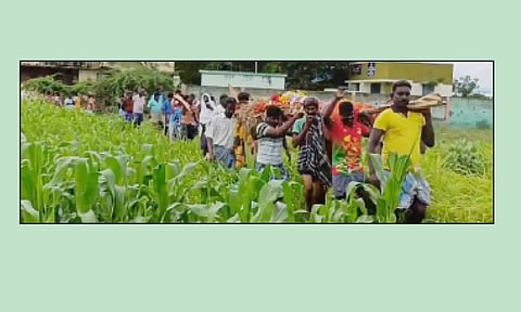 விளைநிலங்கள் வழியாக இறந்தவரிடம் உடலை தூக்கி செல்லும் பொதுமக்கள்.