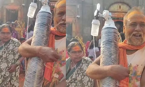 ஆக்சிஜன் சிலிண்டரை சுமந்தபடி மனைவியை கோவிலுக்கு அழைத்து சென்ற விவசாயி- பக்தர்களை நெகிழ வைத்த தம்பதி