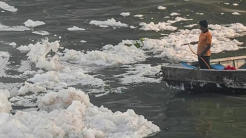 A worker navigates the heavy layer of chemical foam on the Yamuna