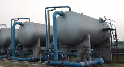 Three large, horizontal silver pressurized tanks connected by an intricate network of blue pipelines at an industrial water treatment site.