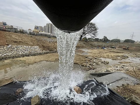 A dynamic photograph looking down the mouth of a very large dark pipe as a heavy volume of clear water gushes out.