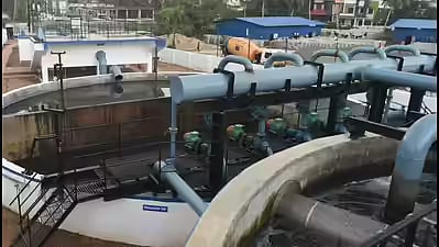 An elevated view of the Muttathara sewage treatment plant in Thiruvananthapuram, featuring large circular filtration tanks, industrial piping, and blue-roofed facility buildings.