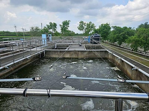 An industrial water treatment facility featuring aeration tanks with bubbling water, metal railings, and infrastructure surrounded by trees under a cloudy sky.