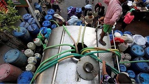 Water tanker filling blue barrels in a crowded Mumbai street.