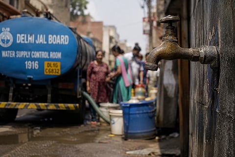 A blue and yellow Delhi Jal Board water tanker truck parked on the side of a road in New Delhi, supplying water during a supply shortage.