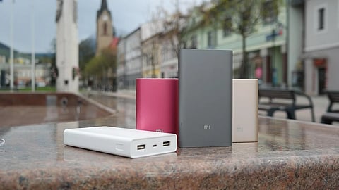Multiple Mi power banks in white, pink, gray, and gold on a stone surface outdoors.