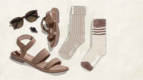 Flat lay of trendy sandals paired with neutral-colored socks, sunglasses, and a watch on a light textured background.