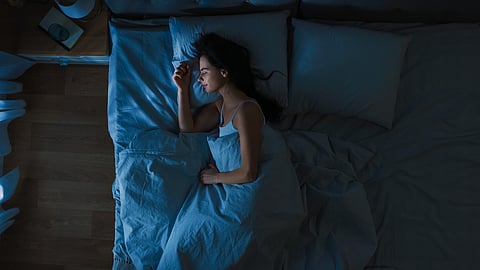 Top View of Beautiful Young Woman Sleeping Cozily on a Bed in her Bedroom at Night. Blue Nightly Colors with Cold Weak Lamppost Light Shining Through the Window.