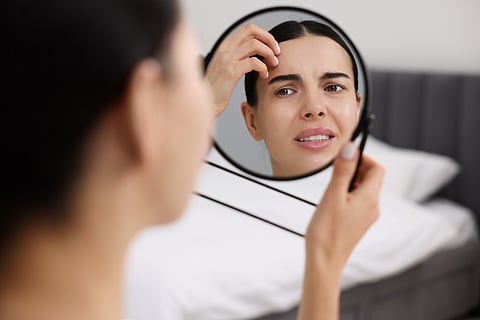 A women looking in mirror and worried about her dull skin.