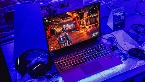 Gaming laptop running a game with RGB backlit keyboard and gaming accessories.